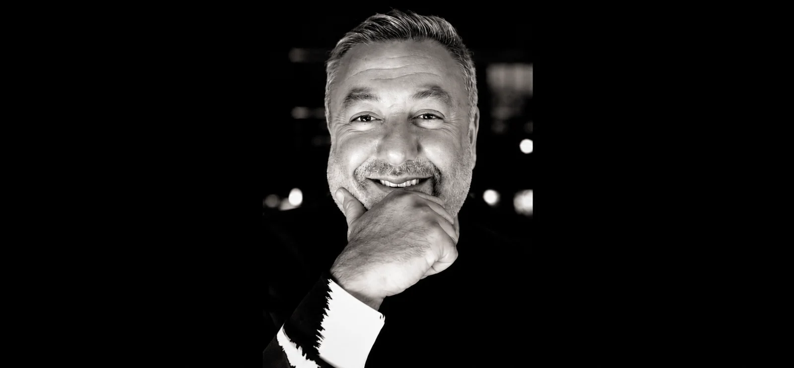 Black and white portrait of Murat Bilican smiling, hand on chin